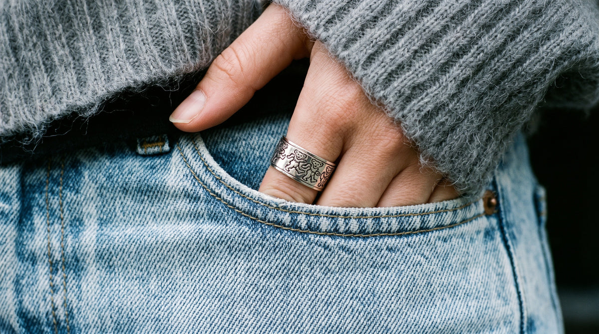 Grateful Dead Dancing Bear sterling silver spinner ring worn on a hand tucked into the pocket of light blue jeans under a grey mohair sweater
